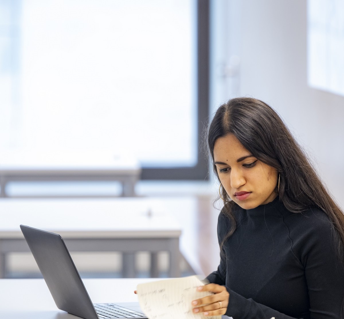 A female student in a dark top is deep in study with paper and laptop